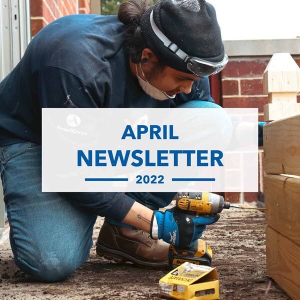 A person using a yellow power drill assembles a wooden structure outdoors. They wear gloves, a mask, and protective goggles. Text overlay reads: “April Newsletter 2022.”.