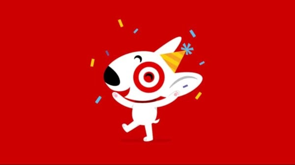 A cheerful white dog with a Target bullseye over its left eye wears a yellow party hat and smiles while confetti falls around it, set against a bright red background.